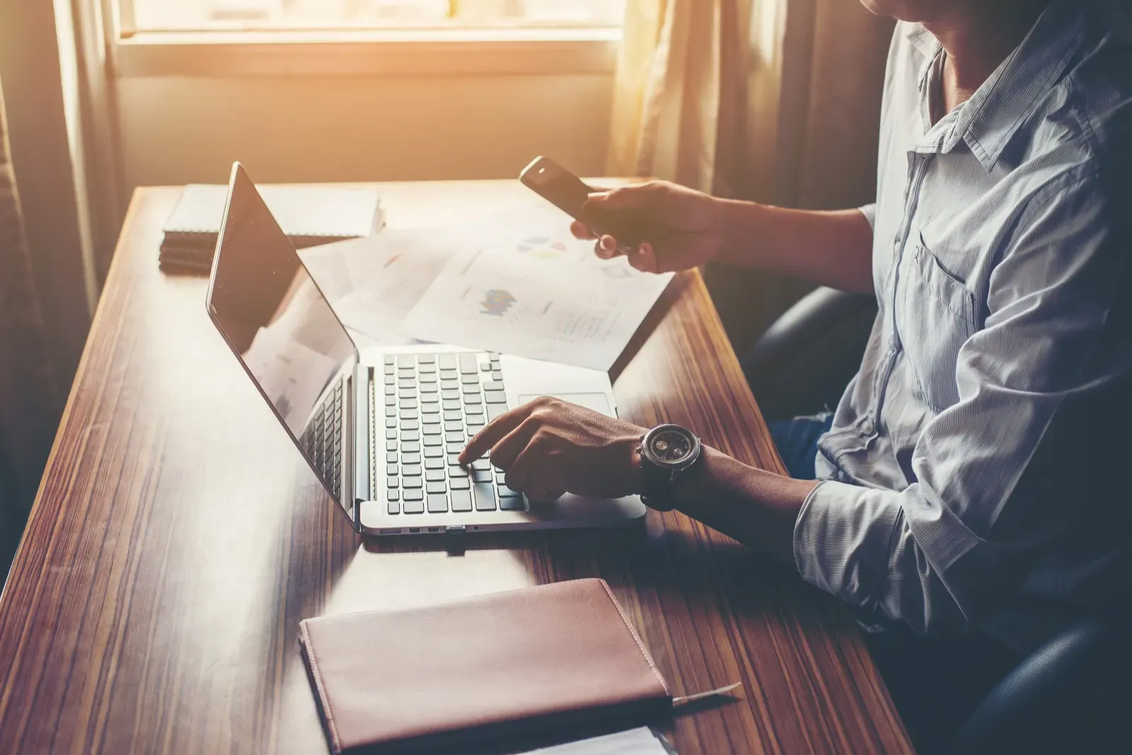 Ofis masasında dizüstü bilgisayar ve akıllı telefon ekranlarına bakan kişi